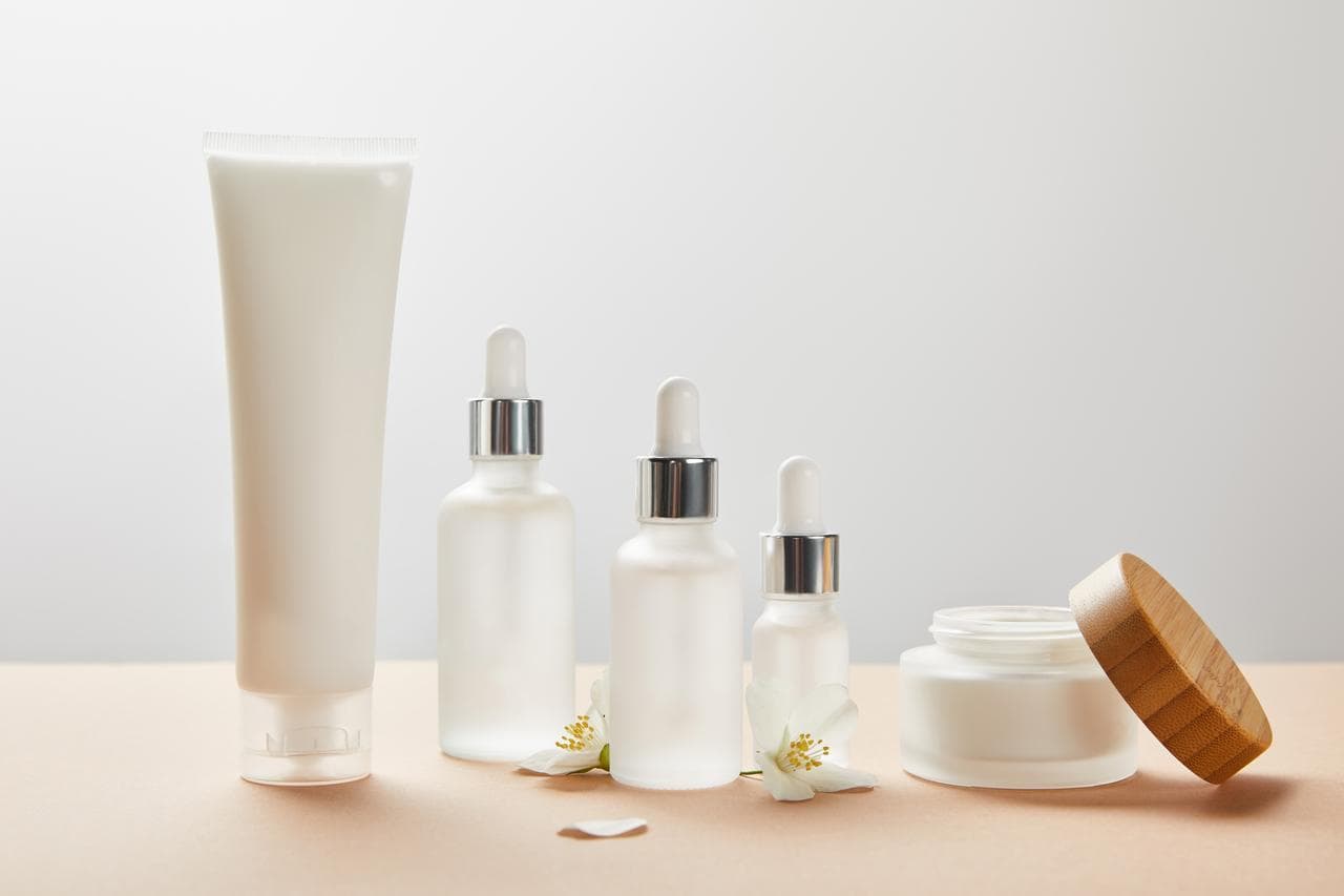 Cream tube, dropper bottles, and a wooden-lidded jar with white blossoms